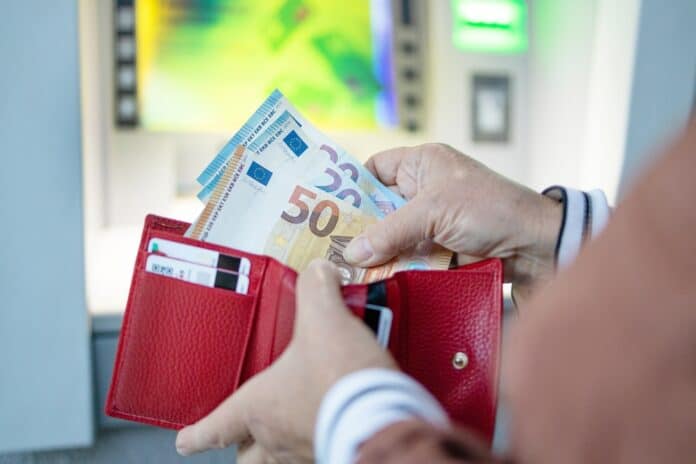 Person putting money from ATM in wallet, source: Shutterstock