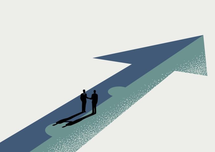 Business partnership, merger and acquisition deal concept, businessmen handshaking on assembled arrow jigsaw, vector illustration, source: Shutterstock