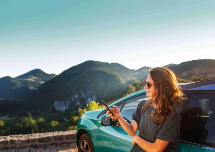 Ayvens, γυναίκα με κινητό και αυτοκίνητο σε εκδρομή στο βουνό, εικόνα μελέτης Car Cost Index 2026