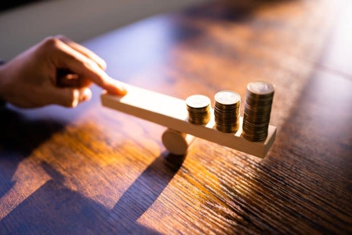 Money Leverage And Economy Balance concept with coins on wooden blocks and hand, source: Shutterstock