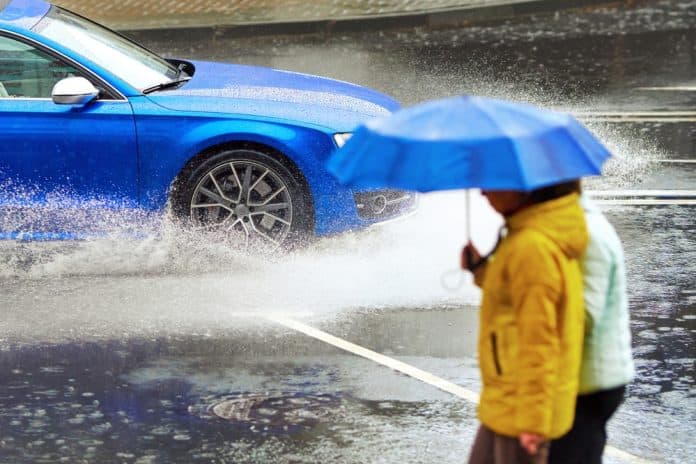 Car in heavy rain and people with umbrella, uninsured car concept, source: Shutterstock