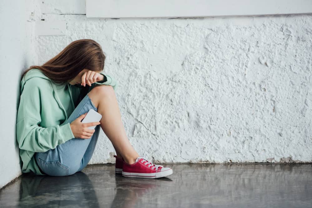 Girl with smartphone crying, cyberbullying concept, source: Shutterstock