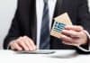 Businessman hand holding wooden home model with Greek flag. insurance and property concept, source: Shutterstock