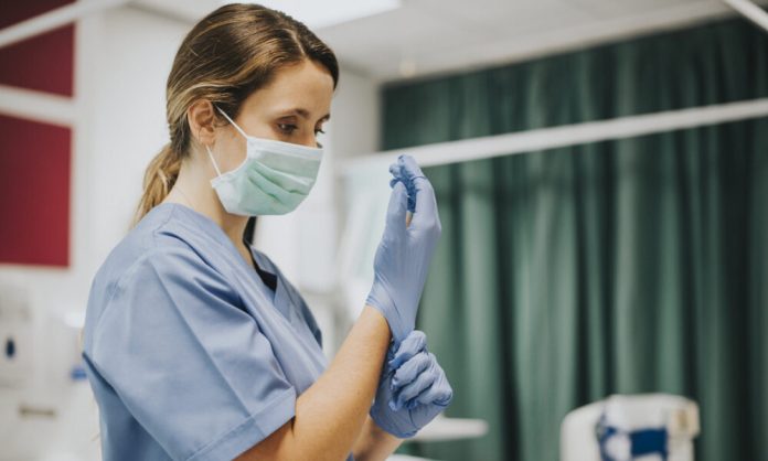 Female nurse with a mask putting on gloves