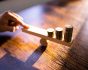 Money Leverage And Economy Balance concept with coins on wooden blocks and hand, source: Shutterstock